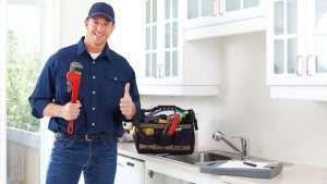 smiling plumber with thumbs up and wrench in kitchen