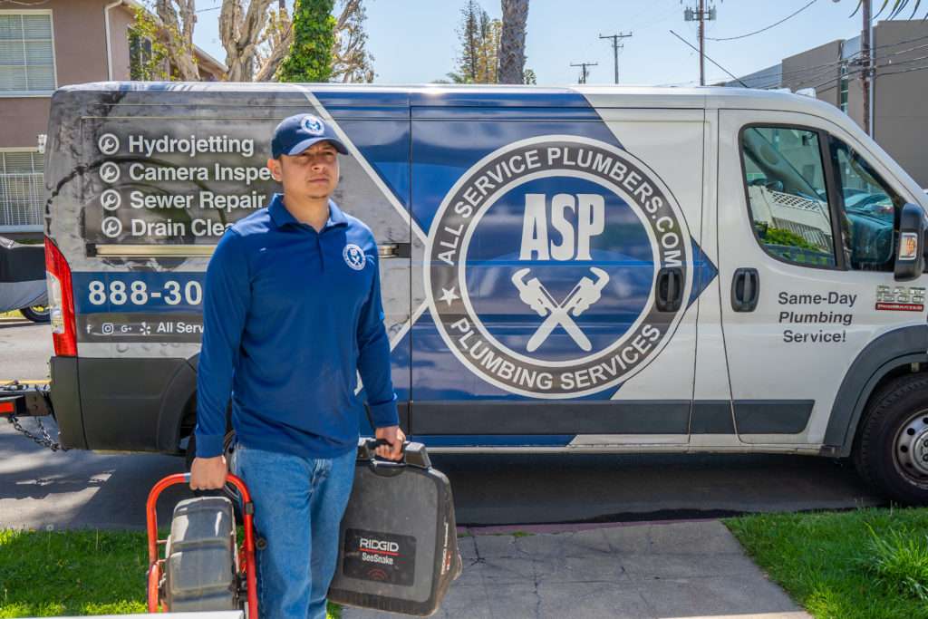 Technician carrying equipment from an All Service Plumbing van